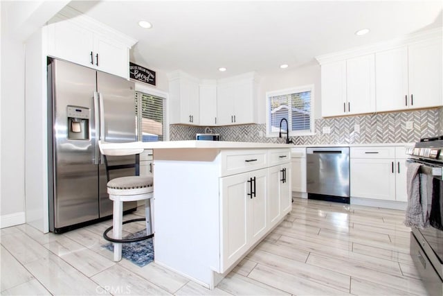 kitchen with a center island, stainless steel appliances, backsplash, a breakfast bar, and white cabinets