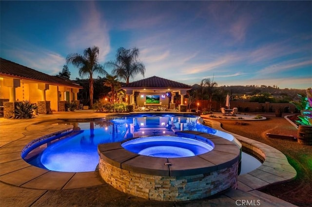 pool at dusk with a patio area and an in ground hot tub