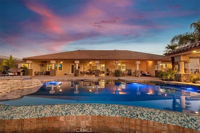 pool at dusk with a jacuzzi and a patio