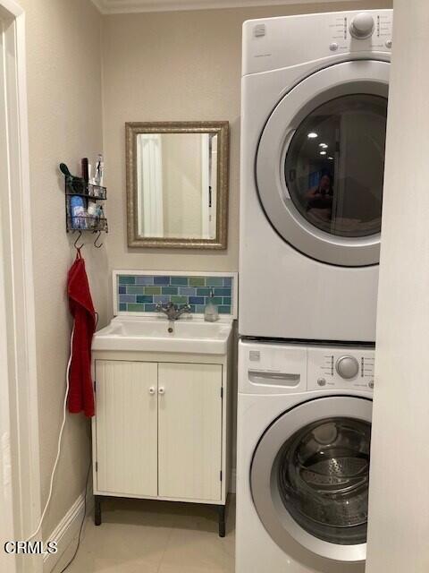 laundry room featuring stacked washer and dryer, cabinets, and sink