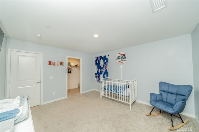 carpeted bedroom featuring a walk in closet and a crib