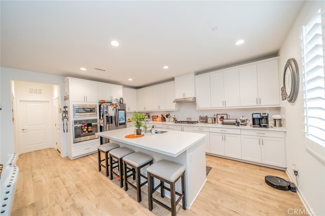 kitchen featuring white cabinetry, light hardwood / wood-style floors, stainless steel appliances, and an island with sink