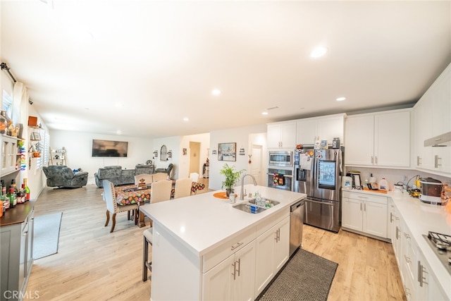 kitchen with appliances with stainless steel finishes, sink, light wood-type flooring, white cabinets, and a center island with sink