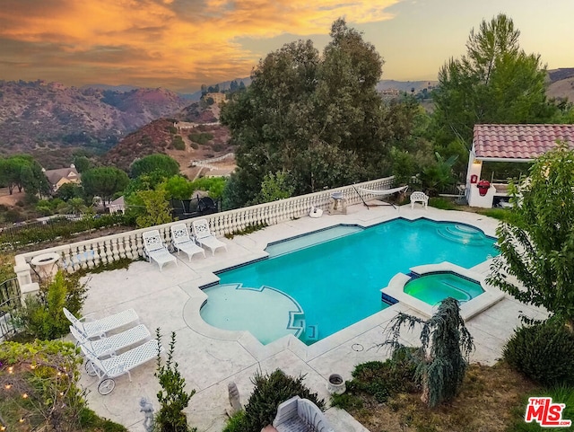 pool at dusk with an in ground hot tub, a mountain view, and a patio area