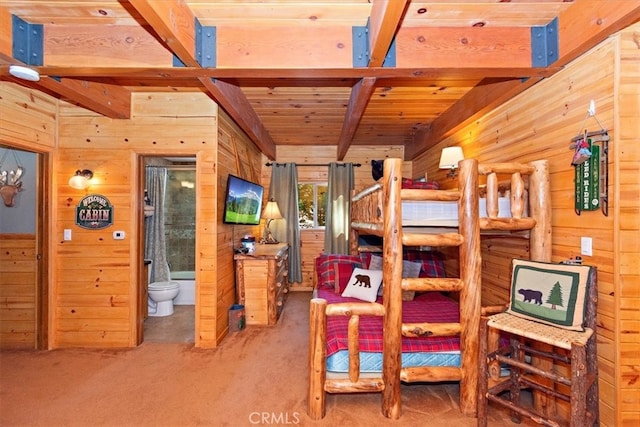 carpeted bedroom with beam ceiling, wood walls, wooden ceiling, and ensuite bathroom