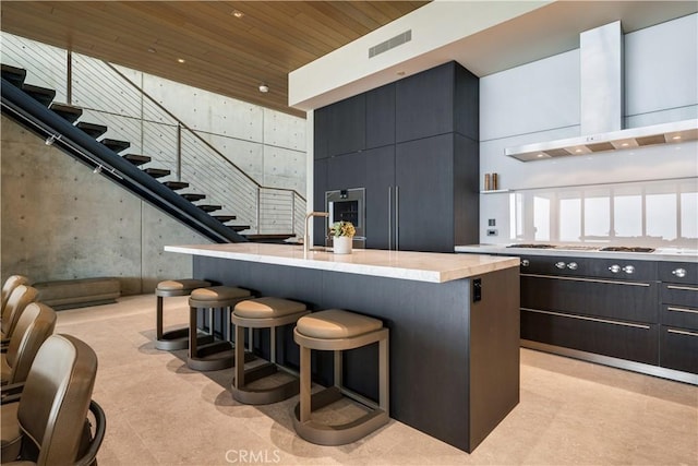 kitchen with a breakfast bar, a kitchen island with sink, exhaust hood, wooden ceiling, and a high ceiling