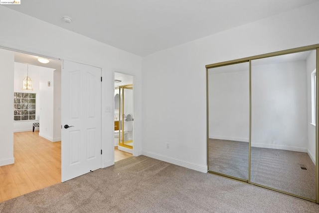 unfurnished bedroom with a closet, ensuite bath, and wood-type flooring