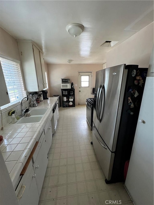 kitchen with black gas range, sink, stainless steel fridge, tile counters, and white cabinetry