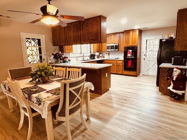 kitchen featuring sink, plenty of natural light, black double oven, light hardwood / wood-style floors, and kitchen peninsula