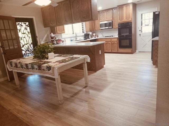 kitchen with black appliances, sink, a kitchen breakfast bar, kitchen peninsula, and light wood-type flooring