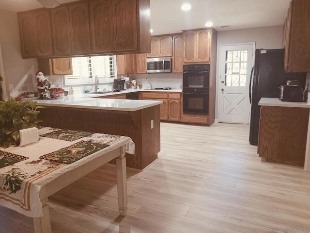 kitchen featuring black appliances, sink, a kitchen bar, light hardwood / wood-style floors, and kitchen peninsula