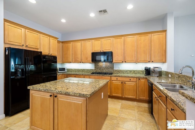 kitchen with black appliances, a center island, light stone counters, and sink