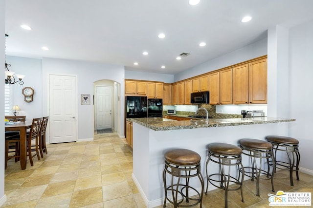 kitchen with kitchen peninsula, a breakfast bar, sink, black appliances, and dark stone countertops