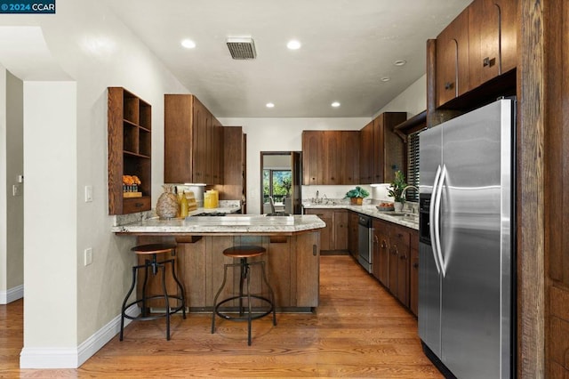 kitchen featuring kitchen peninsula, stainless steel appliances, sink, a breakfast bar, and light wood-type flooring