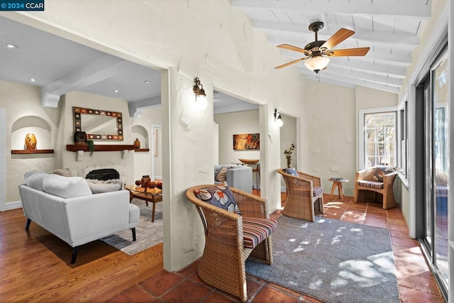 sitting room featuring a stone fireplace, lofted ceiling with beams, hardwood / wood-style flooring, and ceiling fan