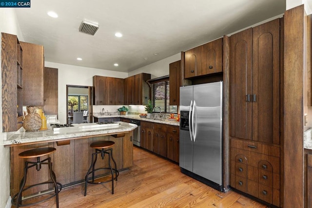 kitchen featuring sink, a kitchen bar, light wood-type flooring, kitchen peninsula, and stainless steel appliances