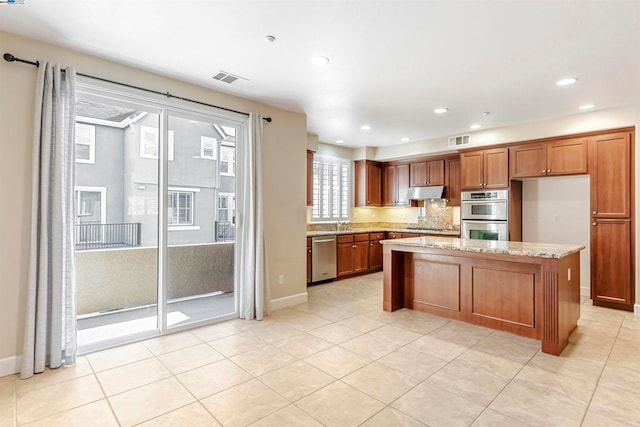 kitchen featuring light stone countertops, sink, a kitchen island, stainless steel appliances, and light tile patterned floors