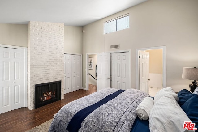 bedroom with a brick fireplace, dark wood-type flooring, a high ceiling, and two closets