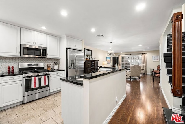 kitchen with appliances with stainless steel finishes, light wood-type flooring, pendant lighting, an inviting chandelier, and white cabinetry