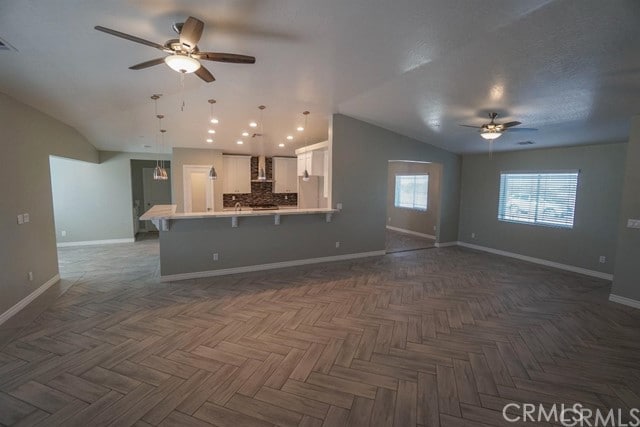 unfurnished living room featuring vaulted ceiling, dark parquet floors, and ceiling fan