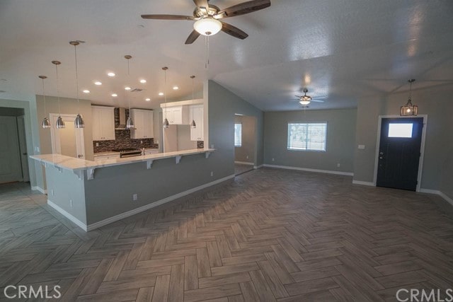 kitchen with decorative backsplash, wall chimney range hood, a kitchen bar, pendant lighting, and white cabinets