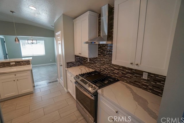 kitchen featuring white cabinets, light stone counters, wall chimney range hood, and stainless steel gas range oven