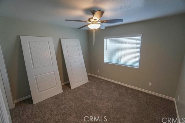 unfurnished bedroom featuring ceiling fan and dark colored carpet