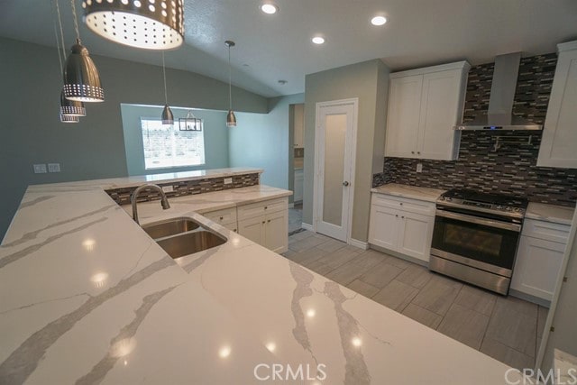 kitchen featuring wall chimney range hood, white cabinets, light stone countertops, vaulted ceiling, and stainless steel gas range