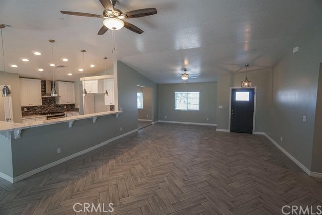 kitchen with backsplash, stainless steel range oven, white cabinetry, wall chimney exhaust hood, and a breakfast bar area