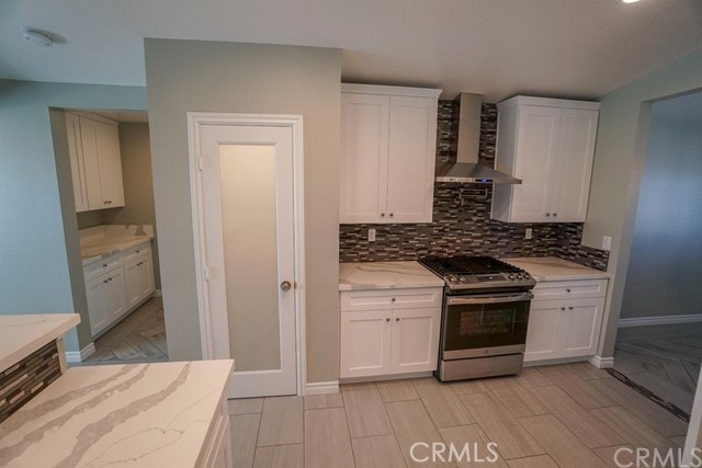 kitchen with white cabinetry, backsplash, wall chimney exhaust hood, and stainless steel gas stove