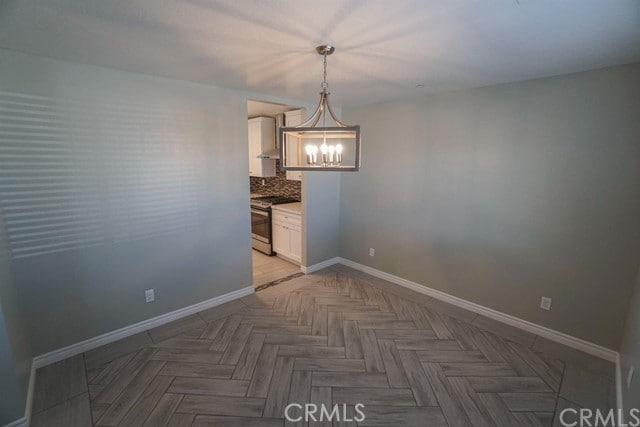 unfurnished dining area featuring parquet flooring and a notable chandelier