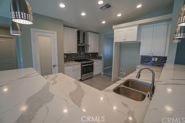 kitchen with wall chimney exhaust hood, light stone counters, and stainless steel range oven