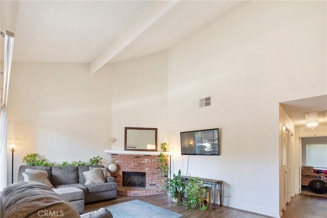 living room featuring visible vents, wood finished floors, a high ceiling, a brick fireplace, and beam ceiling