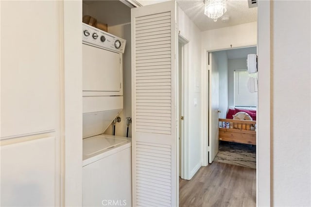 laundry room featuring a textured ceiling, a notable chandelier, laundry area, stacked washer / dryer, and light wood-style floors