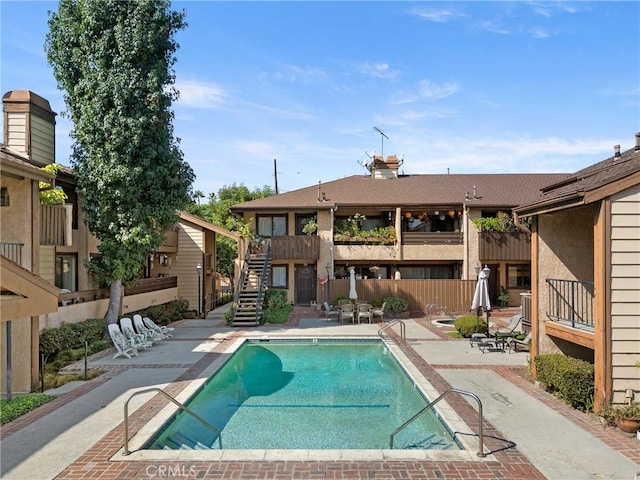 community pool with a patio area, fence, and stairs