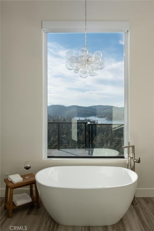 bathroom with a mountain view, an inviting chandelier, a bath, and wood-type flooring