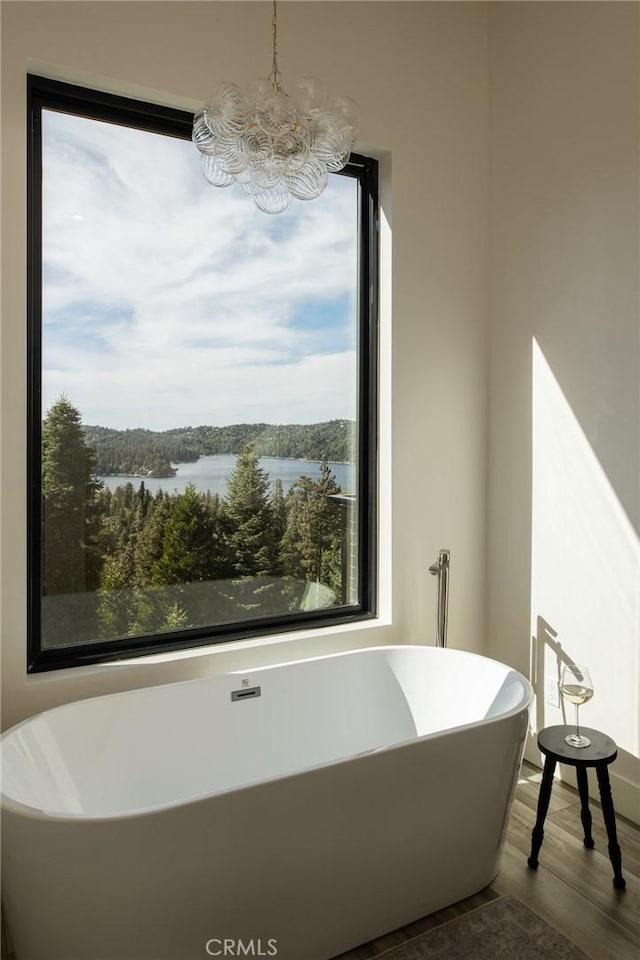 bathroom with hardwood / wood-style flooring, a washtub, a water view, and a chandelier