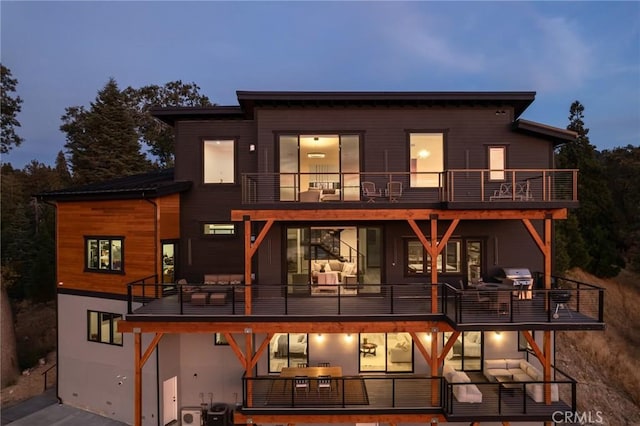 back house at dusk with an outdoor living space, a balcony, and central AC