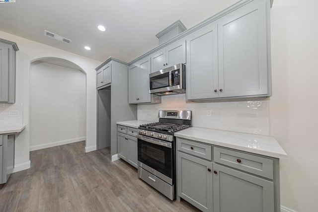 kitchen with stainless steel appliances, light stone countertops, light wood-type flooring, and tasteful backsplash