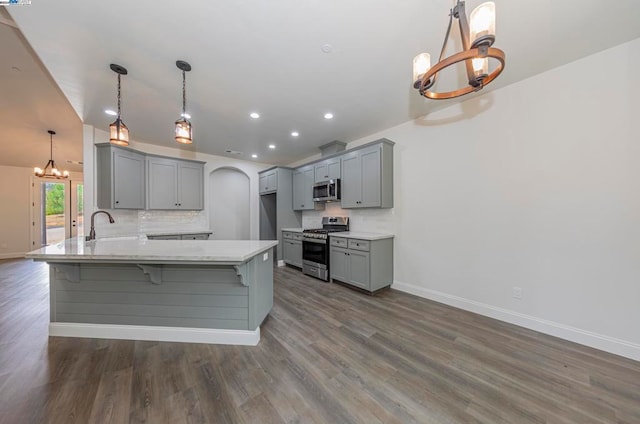 kitchen with hanging light fixtures, appliances with stainless steel finishes, light stone countertops, dark wood-type flooring, and gray cabinets