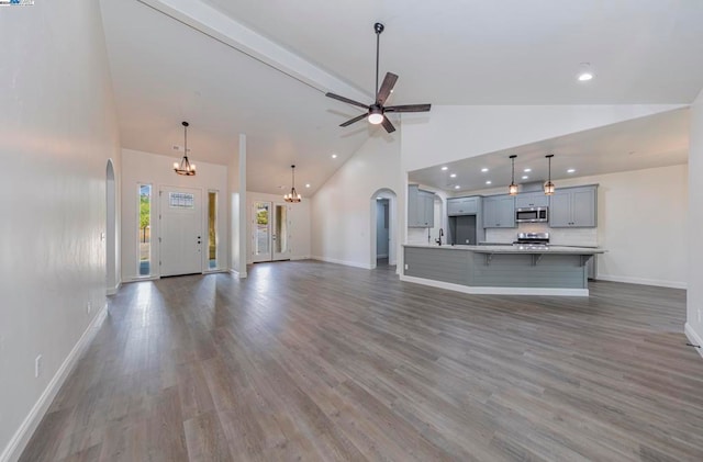 unfurnished living room with dark wood-type flooring, high vaulted ceiling, sink, and ceiling fan with notable chandelier