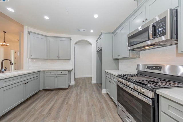 kitchen with appliances with stainless steel finishes, sink, light wood-type flooring, gray cabinets, and decorative backsplash