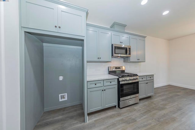 kitchen with gray cabinetry, light hardwood / wood-style floors, stainless steel appliances, and backsplash