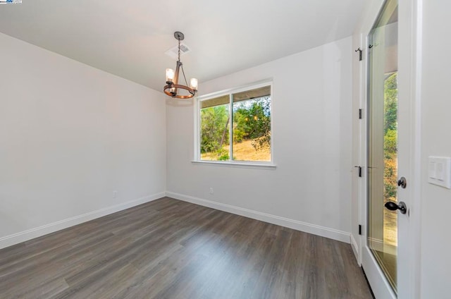 empty room with a notable chandelier and dark hardwood / wood-style floors