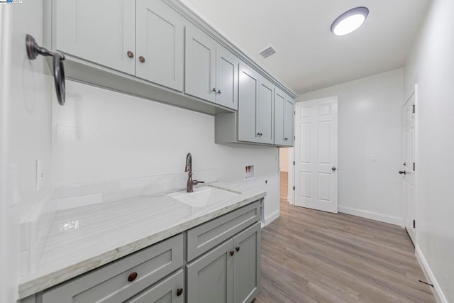 kitchen with light hardwood / wood-style flooring, light stone countertops, sink, and gray cabinetry