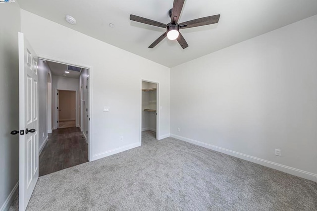 unfurnished bedroom featuring a closet, a spacious closet, carpet flooring, and ceiling fan