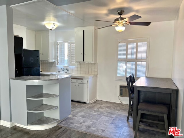 kitchen with wood-type flooring, white cabinetry, ceiling fan, decorative backsplash, and black refrigerator