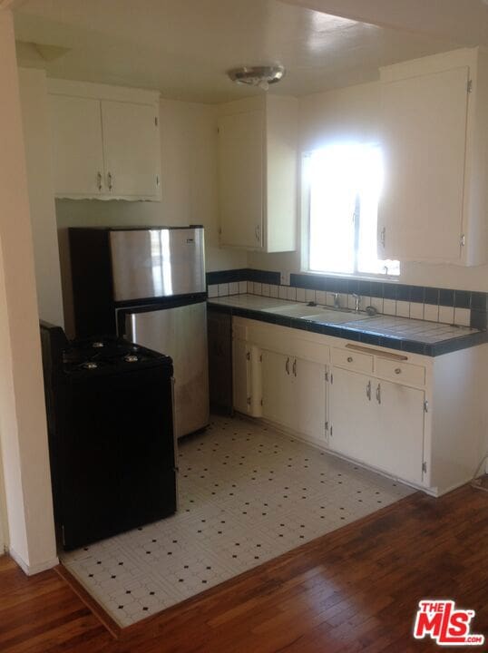 kitchen with stainless steel fridge, black range, white cabinets, and wood-type flooring