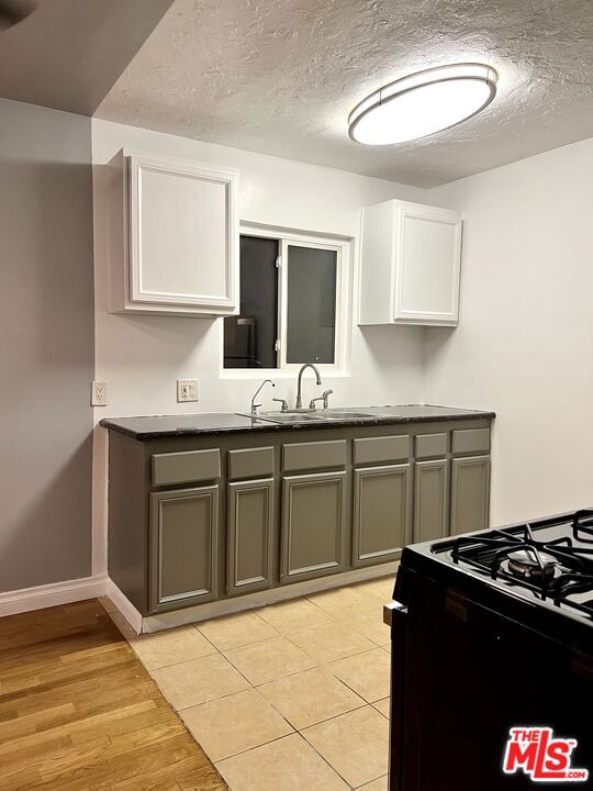 kitchen with black stove, white cabinetry, gray cabinetry, light hardwood / wood-style floors, and sink