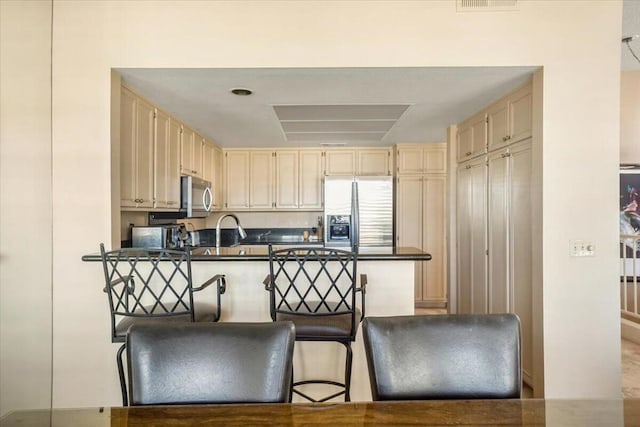 kitchen with appliances with stainless steel finishes, a kitchen breakfast bar, and cream cabinetry